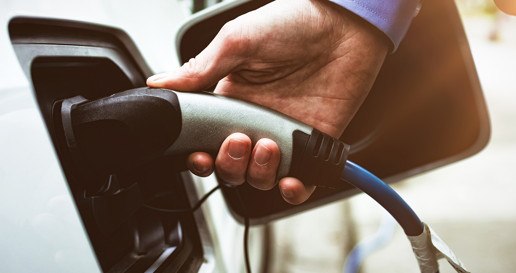 Businessman plugging charger into white electric vehicle