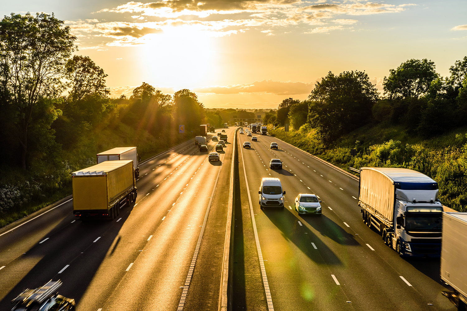 Panoramic view of UK motorway, sunny evening, trees in background, cars, vans and lorries in view