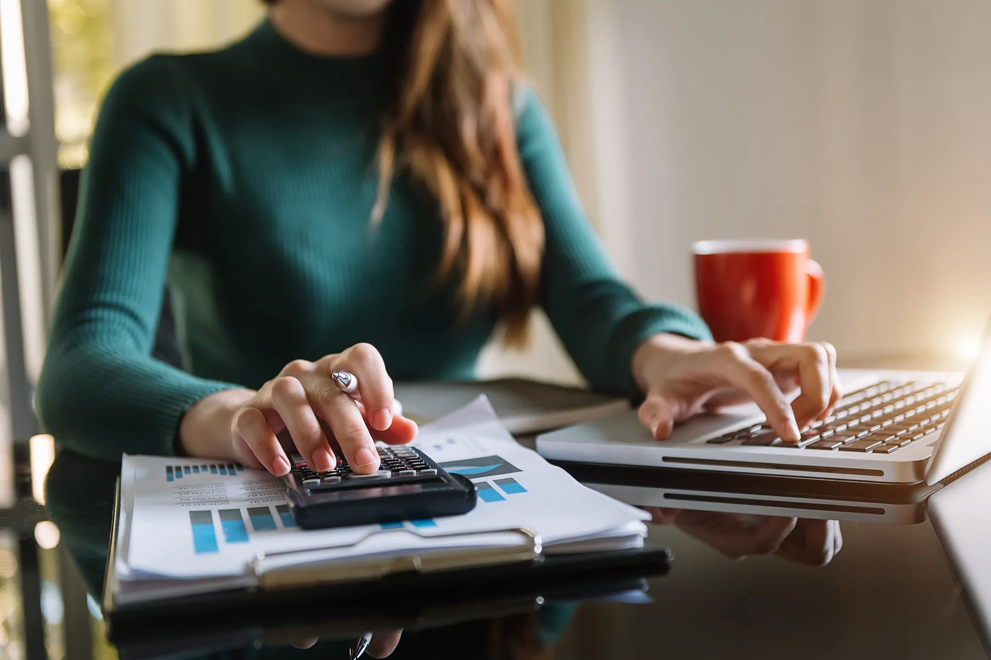 Woman at desk with a lap top, papers and a calculator, to signify accounting