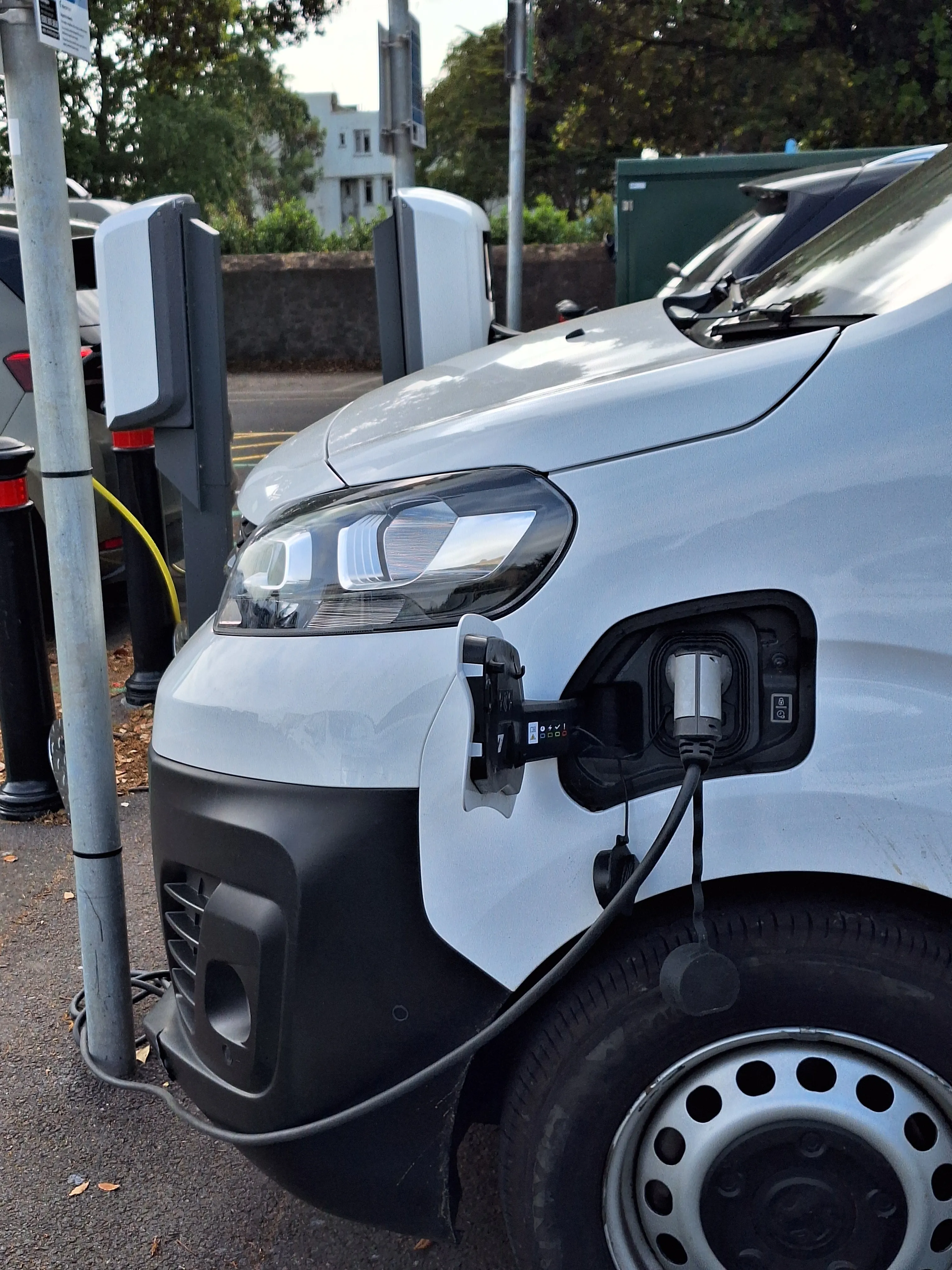 A white e-van charges at a public chargepoint amongst cars