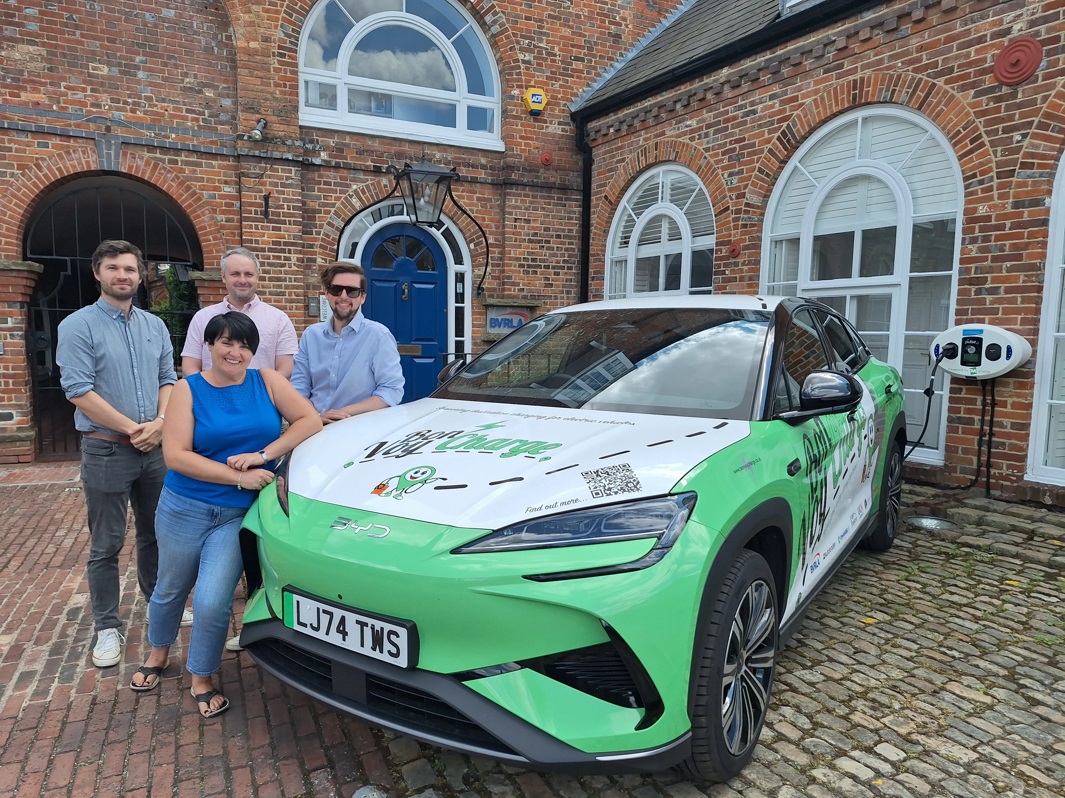 BVRLA team stand next to Bon VoyCharge branded car, coloured in green and white and silver, outside the BVRLA office