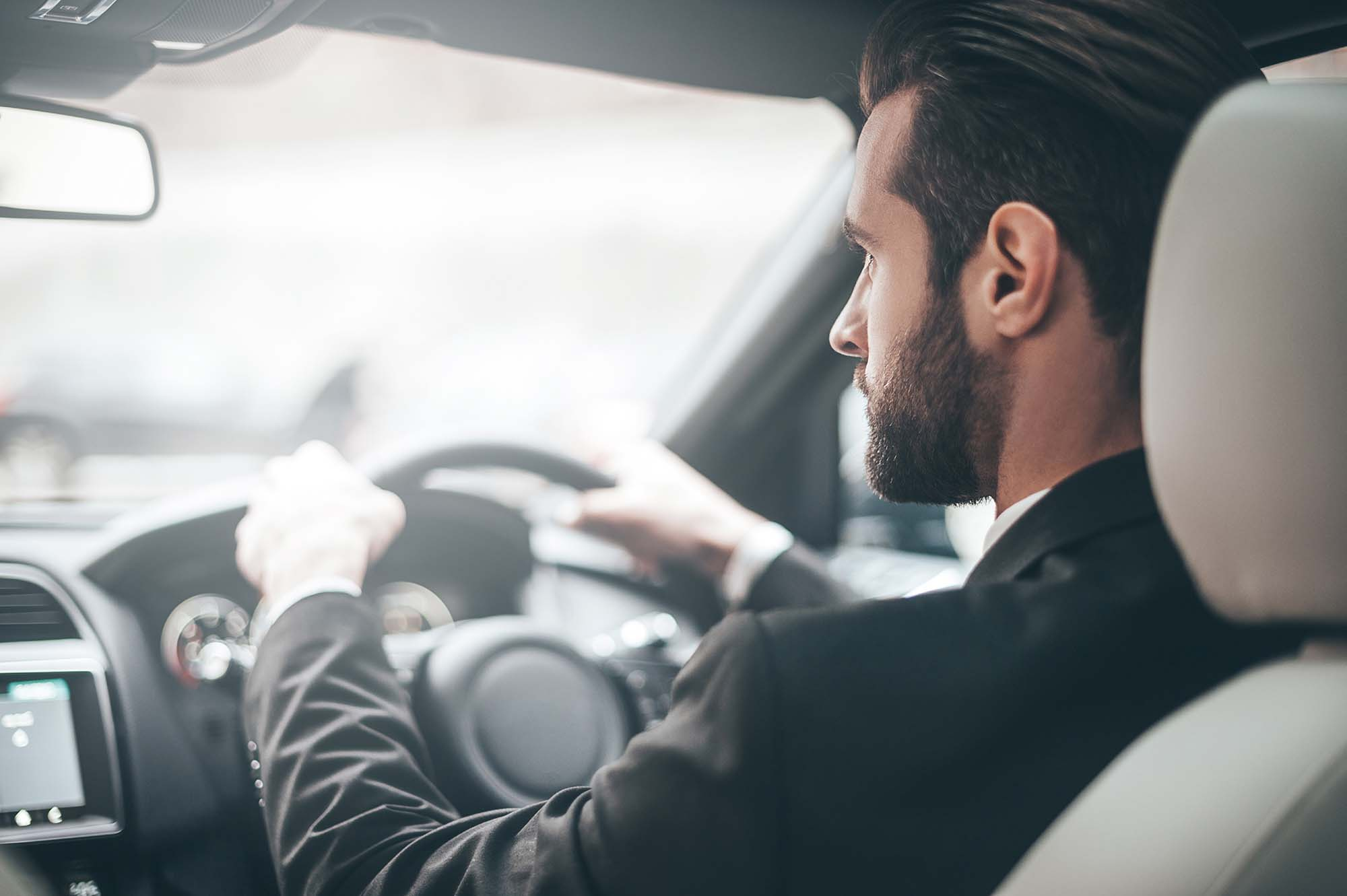 Man in black jacket in a car with hand on steering wheel